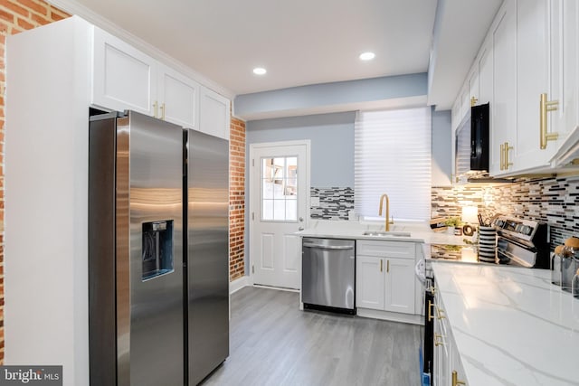 kitchen featuring sink, light hardwood / wood-style flooring, light stone countertops, appliances with stainless steel finishes, and white cabinetry