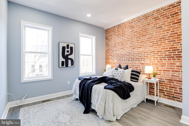 bedroom featuring wood-type flooring and brick wall