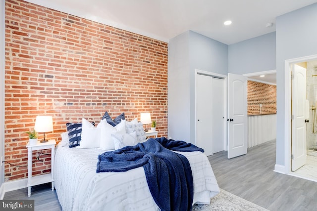 bedroom featuring wood-type flooring, brick wall, and a closet