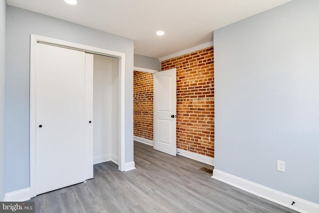 unfurnished bedroom with a closet, brick wall, and wood-type flooring