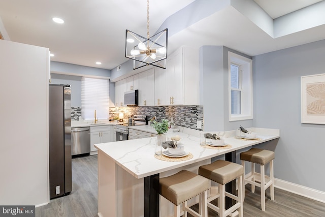 kitchen with sink, kitchen peninsula, pendant lighting, white cabinets, and appliances with stainless steel finishes