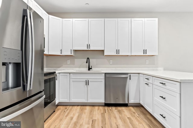 kitchen with white cabinets, light wood-type flooring, stainless steel appliances, and sink