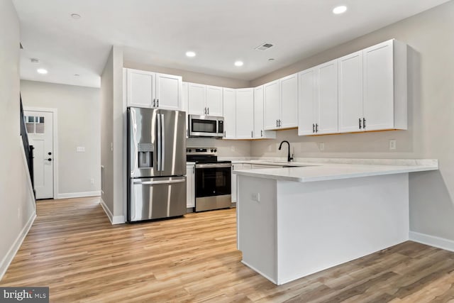 kitchen with white cabinetry, sink, light hardwood / wood-style flooring, kitchen peninsula, and appliances with stainless steel finishes