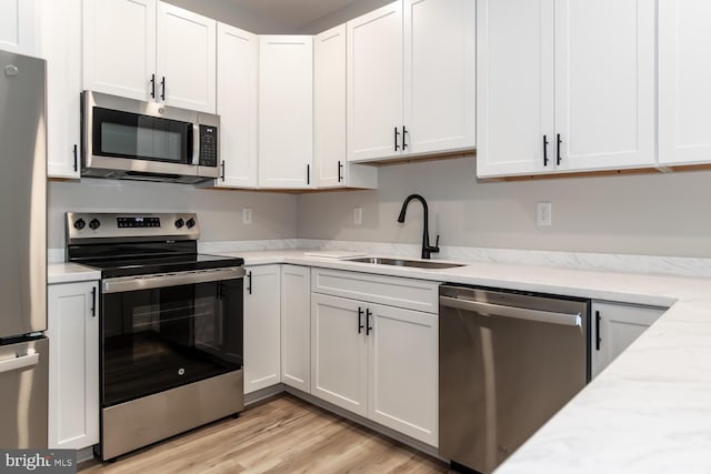 kitchen featuring light stone countertops, sink, stainless steel appliances, light hardwood / wood-style flooring, and white cabinets