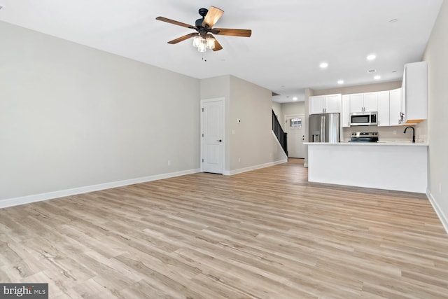 unfurnished living room featuring light hardwood / wood-style floors, ceiling fan, and sink