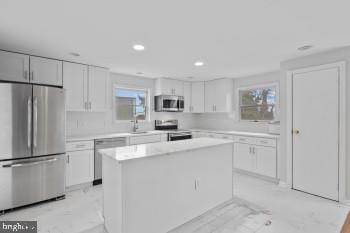 kitchen with white cabinets, stainless steel appliances, a kitchen island, and a wealth of natural light