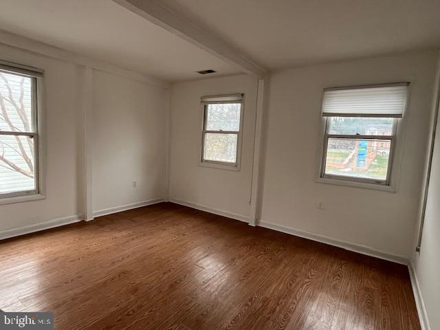 spare room with beamed ceiling, plenty of natural light, and dark wood-type flooring