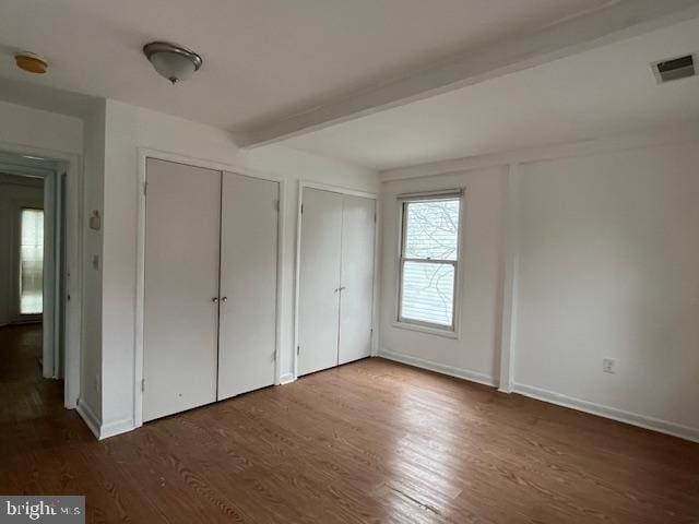 unfurnished bedroom featuring beamed ceiling, dark hardwood / wood-style flooring, and two closets