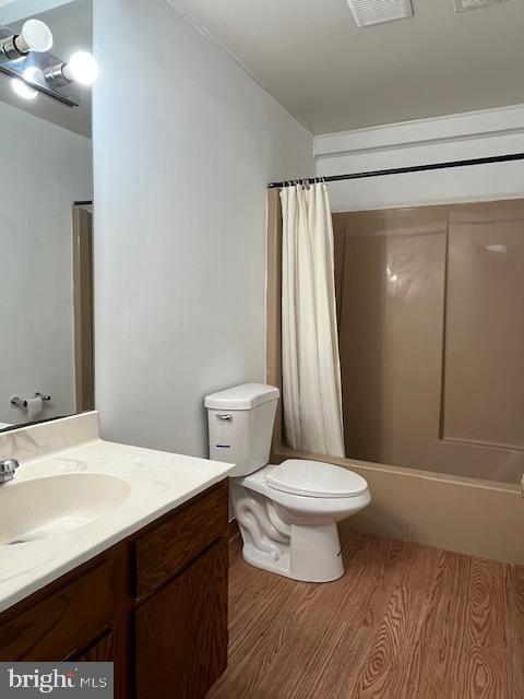 full bathroom with shower / bathtub combination with curtain, hardwood / wood-style floors, vanity, and toilet