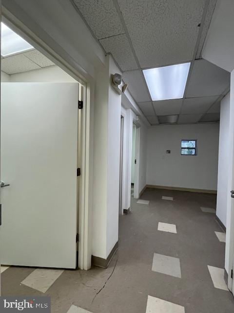 hall with a paneled ceiling and concrete floors