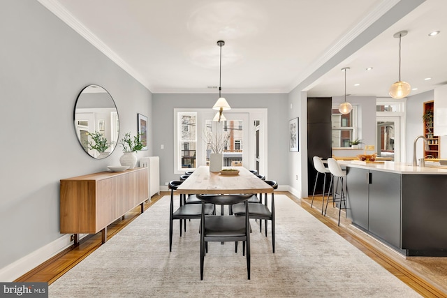 dining space with crown molding, radiator heating unit, sink, and light hardwood / wood-style flooring