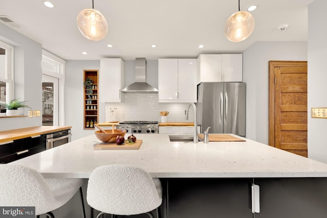 kitchen featuring hanging light fixtures, white cabinets, wall chimney range hood, and stainless steel appliances