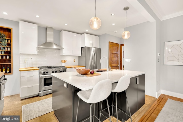 kitchen featuring pendant lighting, wall chimney exhaust hood, white cabinetry, a kitchen island with sink, and stainless steel appliances