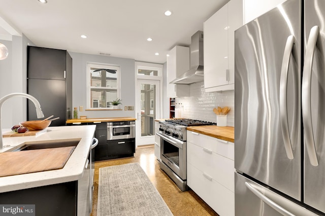 kitchen with tasteful backsplash, white cabinetry, wall chimney range hood, sink, and stainless steel appliances