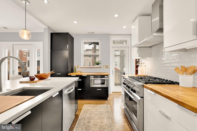 kitchen with pendant lighting, sink, white cabinets, wall chimney range hood, and stainless steel appliances