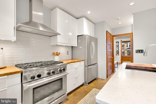 kitchen with wall chimney exhaust hood, sink, white cabinets, decorative backsplash, and stainless steel appliances