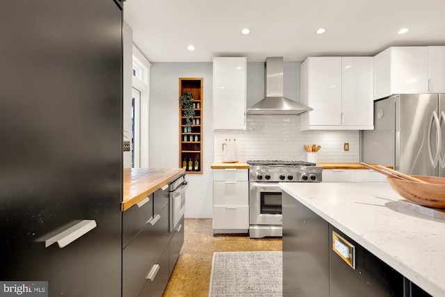 kitchen with white cabinetry, wall chimney range hood, stainless steel appliances, decorative backsplash, and butcher block countertops