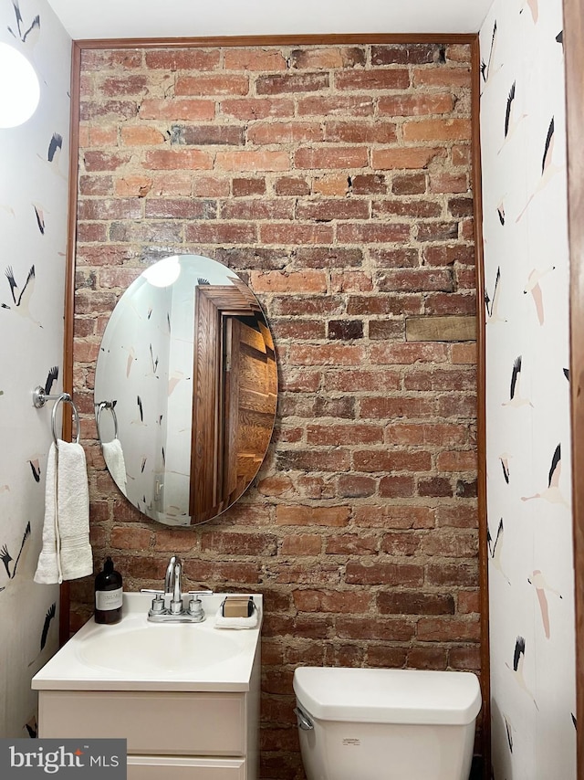 bathroom with toilet, brick wall, and vanity