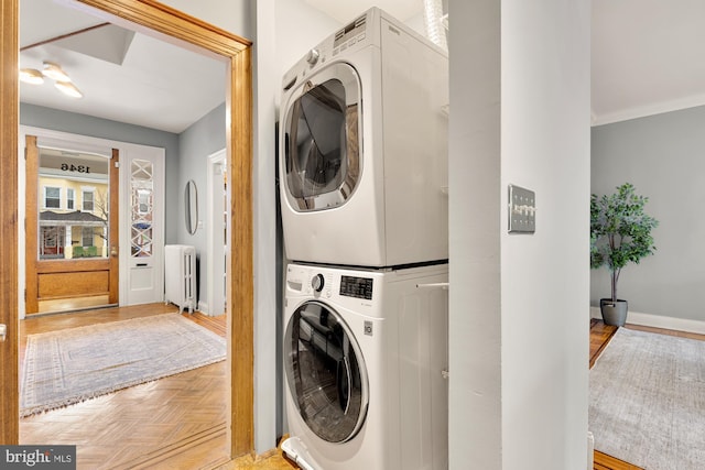 laundry area with light parquet flooring, radiator heating unit, crown molding, and stacked washer and dryer