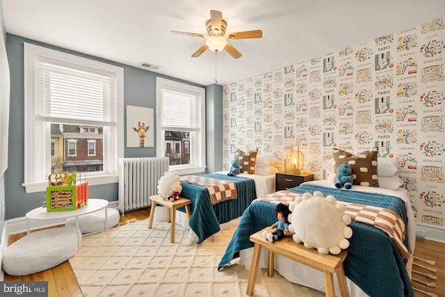 bedroom with ceiling fan, radiator heating unit, light hardwood / wood-style floors, and multiple windows