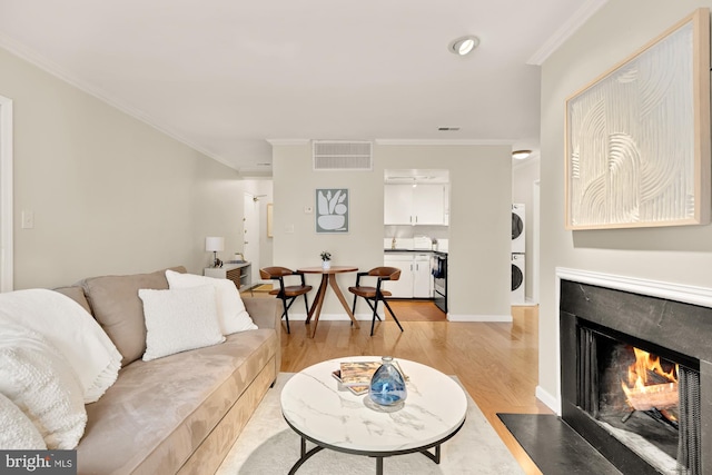 living room with stacked washer and clothes dryer, light hardwood / wood-style floors, and ornamental molding