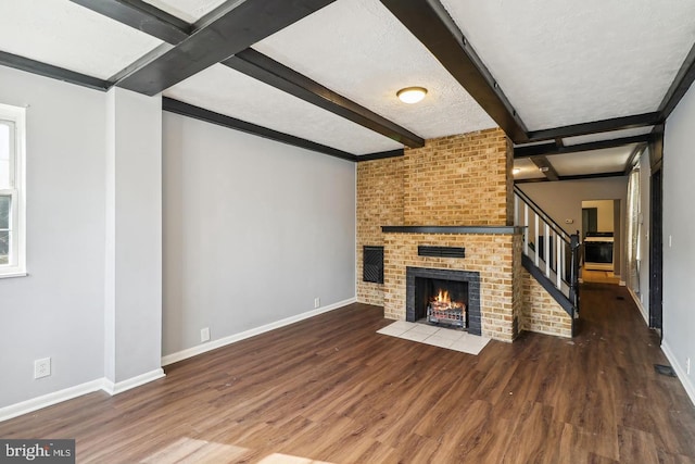 unfurnished living room featuring beam ceiling, a fireplace, dark wood-type flooring, and a textured ceiling