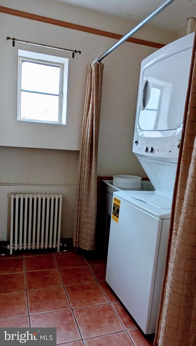 laundry room featuring tile patterned floors, radiator heating unit, and stacked washer and clothes dryer