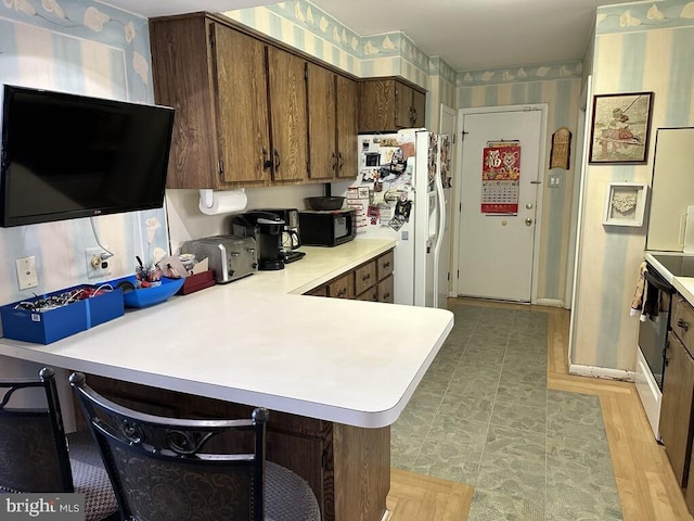 kitchen with kitchen peninsula, a kitchen breakfast bar, light wood-type flooring, range, and white fridge with ice dispenser