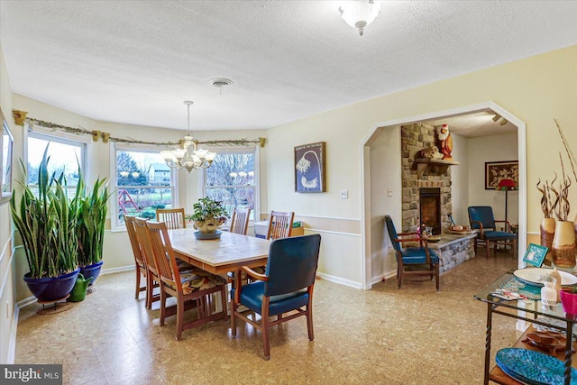 dining area featuring a fireplace, a healthy amount of sunlight, a textured ceiling, and a notable chandelier