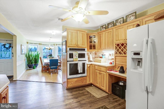 kitchen featuring ceiling fan with notable chandelier, double oven, dark wood-type flooring, white refrigerator with ice dispenser, and pendant lighting