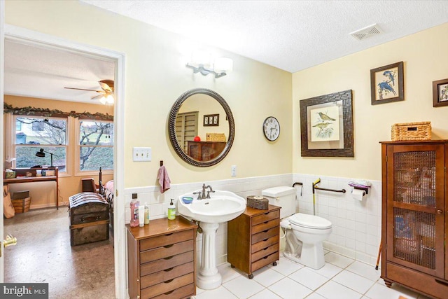 bathroom with ceiling fan, tile patterned floors, a textured ceiling, toilet, and tile walls