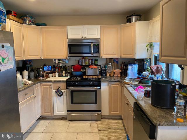 kitchen featuring appliances with stainless steel finishes, light tile patterned floors, white cabinetry, and dark stone counters