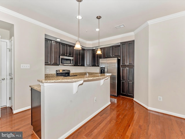 kitchen with appliances with stainless steel finishes, dark hardwood / wood-style flooring, light stone counters, ornamental molding, and hanging light fixtures