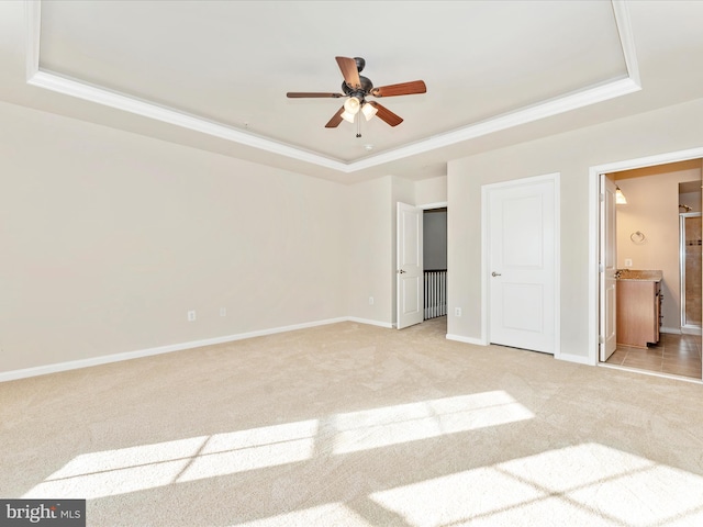 unfurnished bedroom with light carpet, a raised ceiling, ceiling fan, crown molding, and connected bathroom