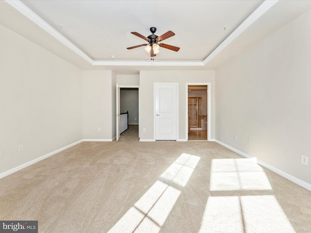 unfurnished bedroom with a tray ceiling, ensuite bath, light carpet, and ceiling fan