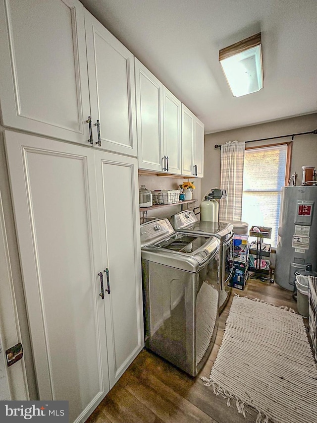 clothes washing area featuring washer and clothes dryer, water heater, dark hardwood / wood-style flooring, and cabinets