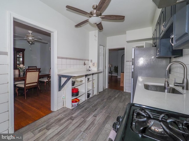 kitchen with blue cabinetry, sink, wood-type flooring, black gas range oven, and ceiling fan