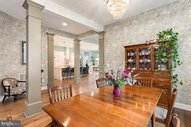 dining room featuring decorative columns, sink, beam ceiling, light hardwood / wood-style flooring, and a chandelier