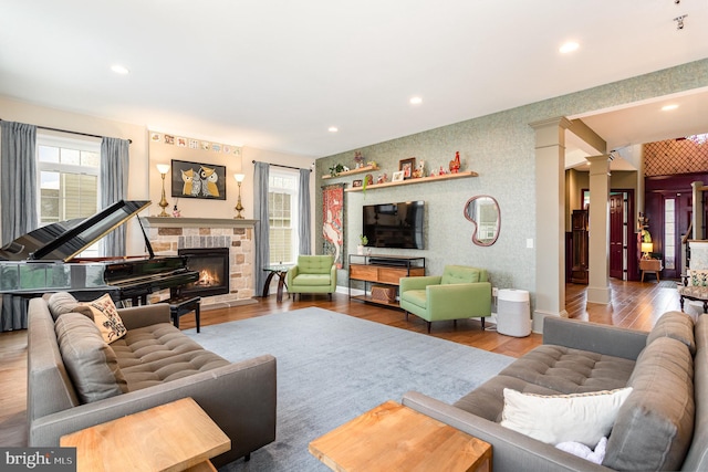 living room featuring a healthy amount of sunlight, wood-type flooring, ornate columns, and a fireplace