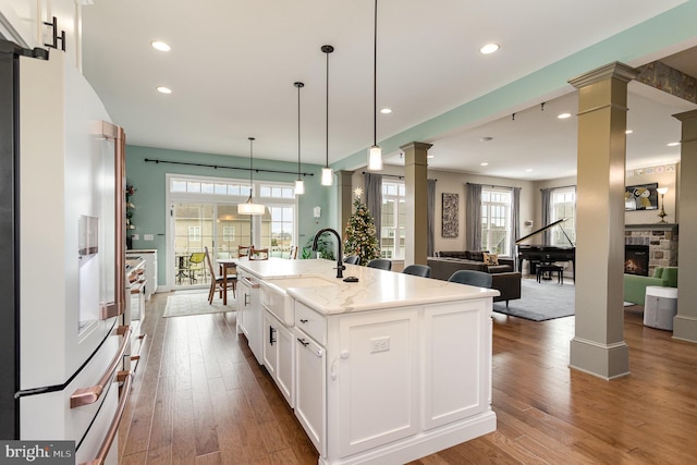 kitchen featuring white cabinetry, white fridge with ice dispenser, hanging light fixtures, a kitchen island with sink, and a fireplace