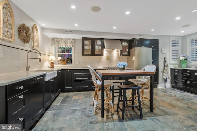 kitchen with backsplash, wall chimney range hood, sink, and stainless steel refrigerator