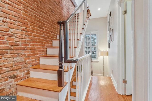 stairs with hardwood / wood-style floors and brick wall