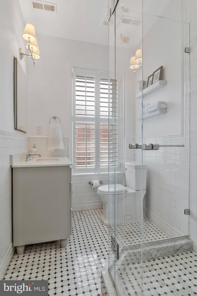 bathroom featuring vanity, tile patterned floors, toilet, tile walls, and a shower with shower door