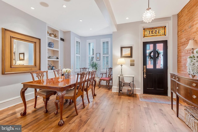 dining area featuring light wood-type flooring, built in features, and an inviting chandelier