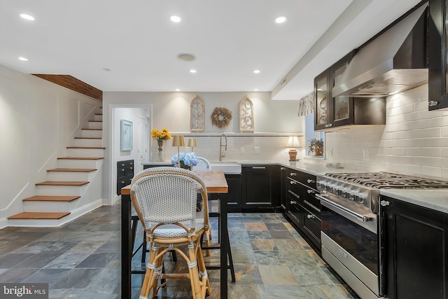 kitchen with tasteful backsplash, sink, stainless steel stove, and wall chimney range hood