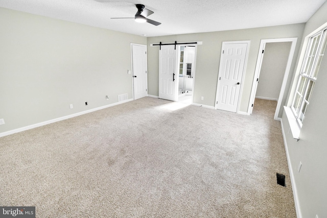 unfurnished bedroom featuring light carpet, ensuite bath, a textured ceiling, ceiling fan, and a barn door