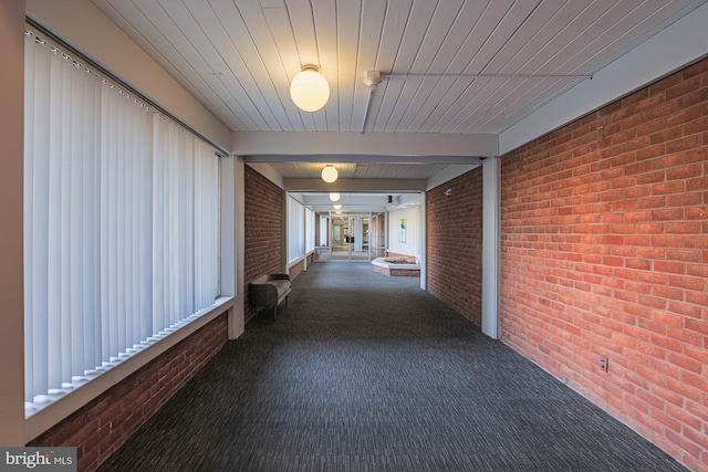 corridor featuring brick wall and dark colored carpet