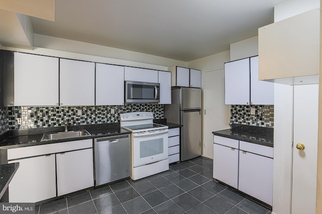 kitchen featuring dark tile patterned flooring, sink, decorative backsplash, appliances with stainless steel finishes, and white cabinetry