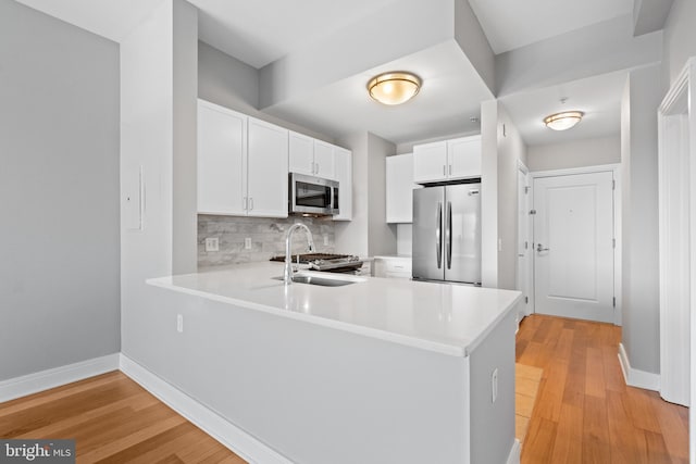 kitchen featuring kitchen peninsula, white cabinetry, stainless steel appliances, and light wood-type flooring