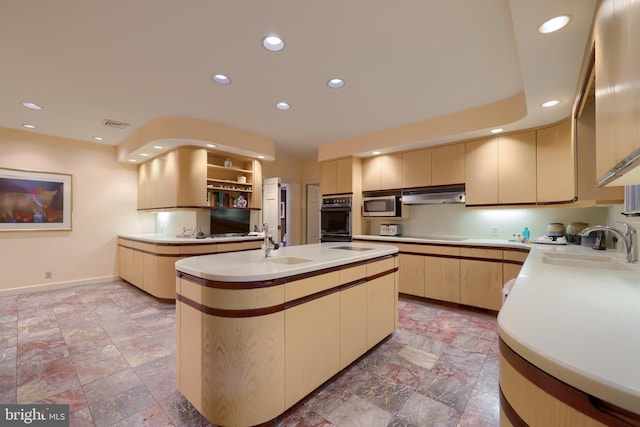 kitchen with light brown cabinetry, black double oven, a center island with sink, and sink